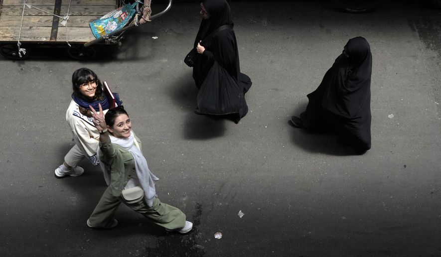 FILE - An Iranian woman without wearing her mandatory Islamic headscarf flashes a victory sign as two head-to-toe veiled women walk at the old main bazaar of Tehran, Iran, June 13, 2024. (AP Photo/Vahid Salemi, File)