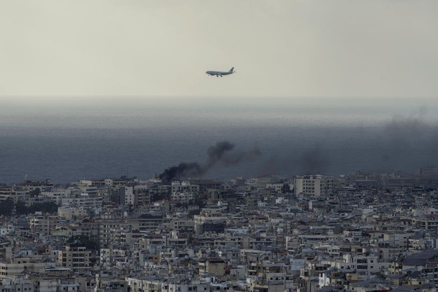 A Middle East Airlines airplane flies over Beirut as smoke rises from Dahiyeh, in Beirut, Lebanon, Tuesday, Oct. 1, 2024. (AP Photo/Bilal Hussein)