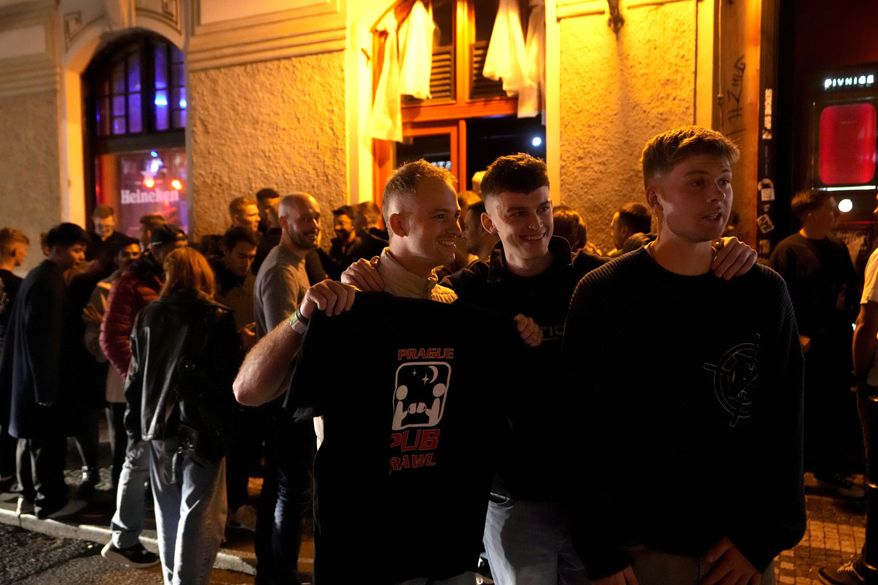 A group of tourists stand in line outside a bar as they attend a pub crawl tour in downtown Prague, Czech Republic, Thursday, Oct. 17, 2024. (AP Photo/Petr David Josek)