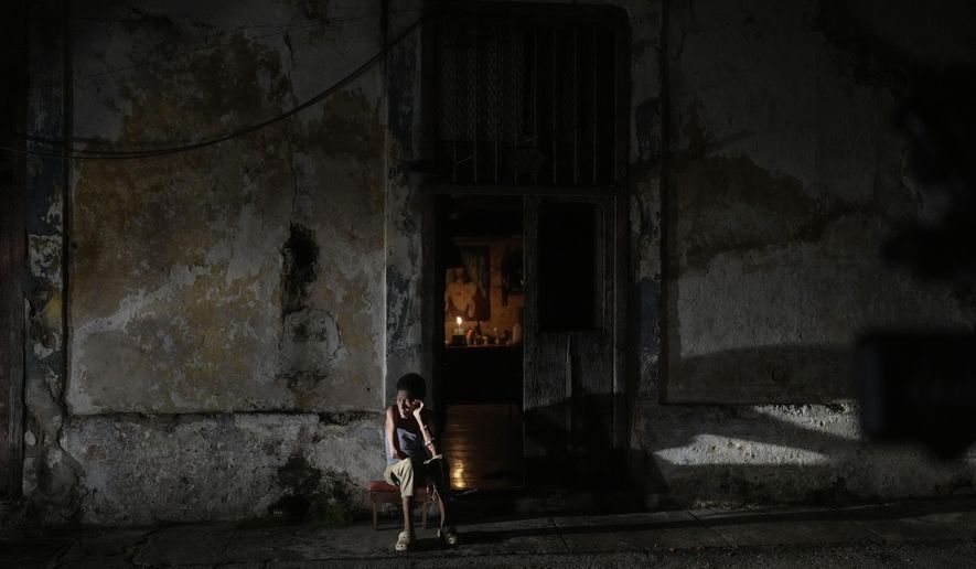 A resident sits while passing time during a blackout following the failure of a major power plant in Havana, Cuba, Saturday, Oct. 19, 2024. (AP Photo/Ramon Espinosa)