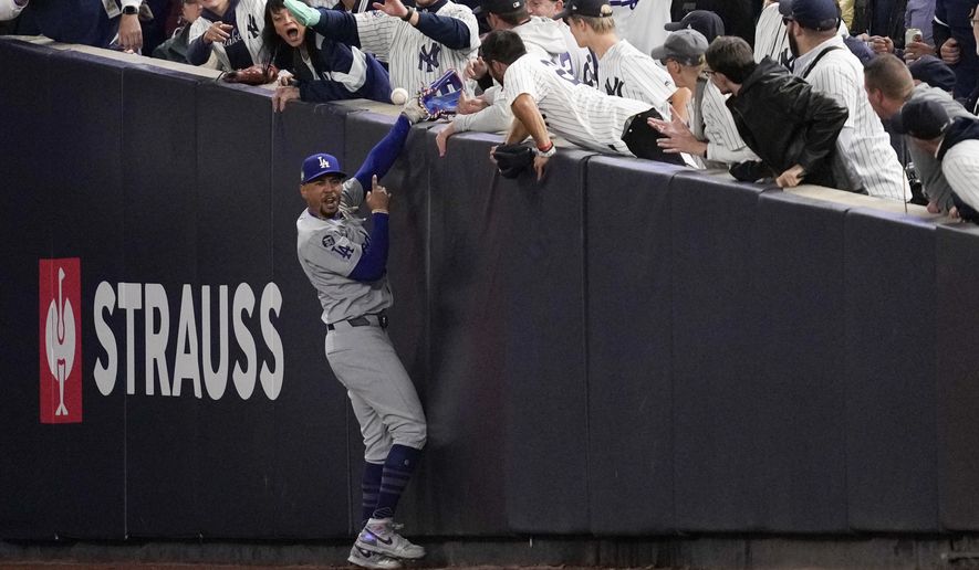 Fans interfere with a foul ball caught by Los Angeles Dodgers right fielder Mookie Betts during the first inning in Game 4 of the baseball World Series against the New York Yankees, Tuesday, Oct. 29, 2024, in New York. (AP Photo/Ashley Landis)