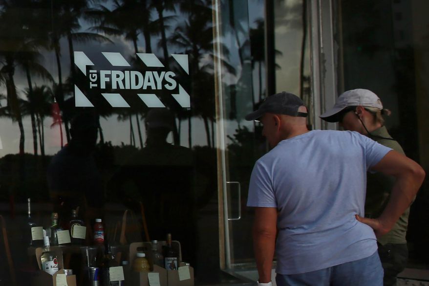 People peek into a window of a TGI Friday's restaurant to see what they are serving to-go on Wednesday, March 25, 2020, in Miami Beach, Fla. (AP Photo/Brynn Anderson, File)