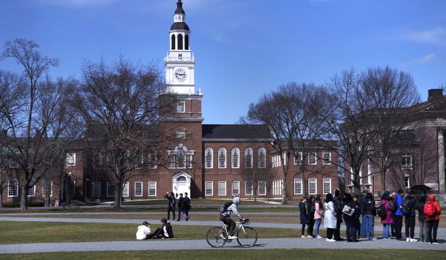A bicyclist passes a college tour group outside the Baker Library at Dartmouth College, April 7, 2023, in Hanover, N.H. (AP Photo/Charles Krupa, File)