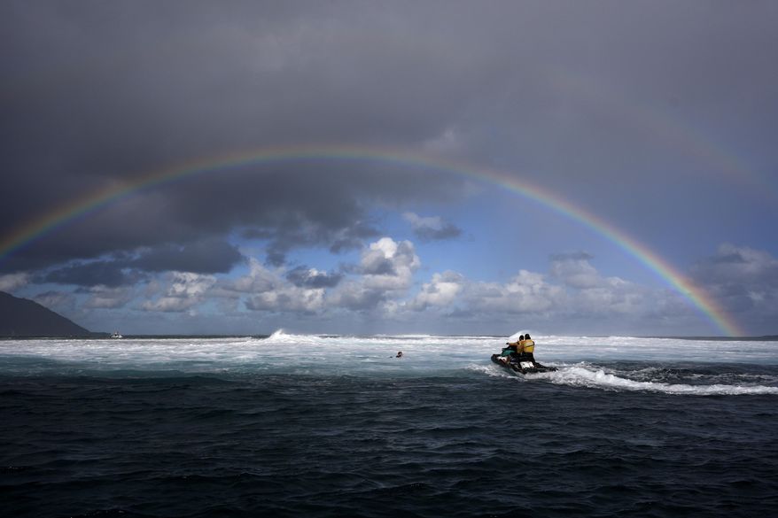 Members of the water safety team move into the impact zone on a jet ski to rescue a surfer under a rainbow during a training day ahead of the 2024 Summer Olympics surfing competition in Teahupo'o, Tahiti, on July 23, 2024. (AP Photo/Gregory Bull)