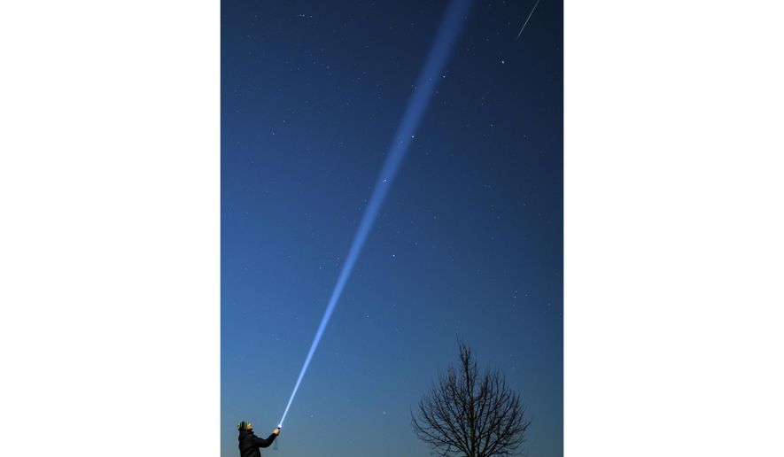 A shooting star, top right, is seen over eastern Brandenburg, Germany, while a person shines a flashlight into the night sky, Saturday, Dec. 14, 2024. (Patrick Pleul/dpa via AP)