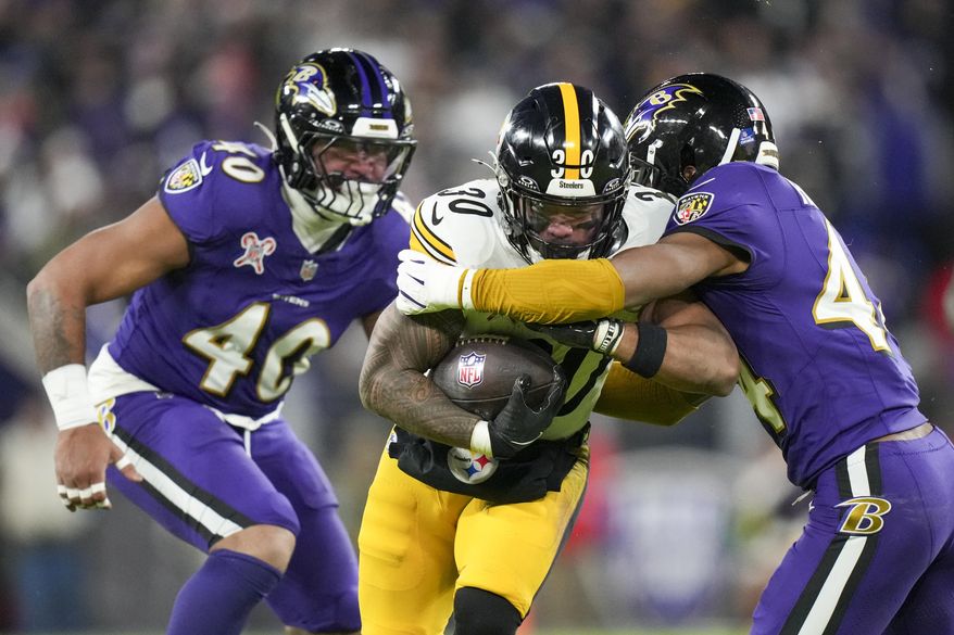 Pittsburgh Steelers running back Jaylen Warren (30) runs with the ball as Baltimore Ravens cornerback Marlon Humphrey, right, and linebacker Malik Harrison try to stop him during the first half of an NFL football game, Saturday, Dec. 21, 2024, in Baltimore. (AP Photo/Stephanie Scarbrough)