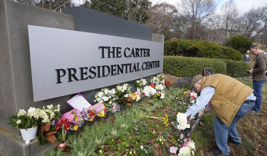 Tom Chaffin, of Atlanta, leaves flowers at the entrance to the Jimmy Carter Presidential Center Tuesday, Dec. 31, 2024, in Atlanta. Carter died Sunday at he age of 100. (AP Photo/John Bazemore )