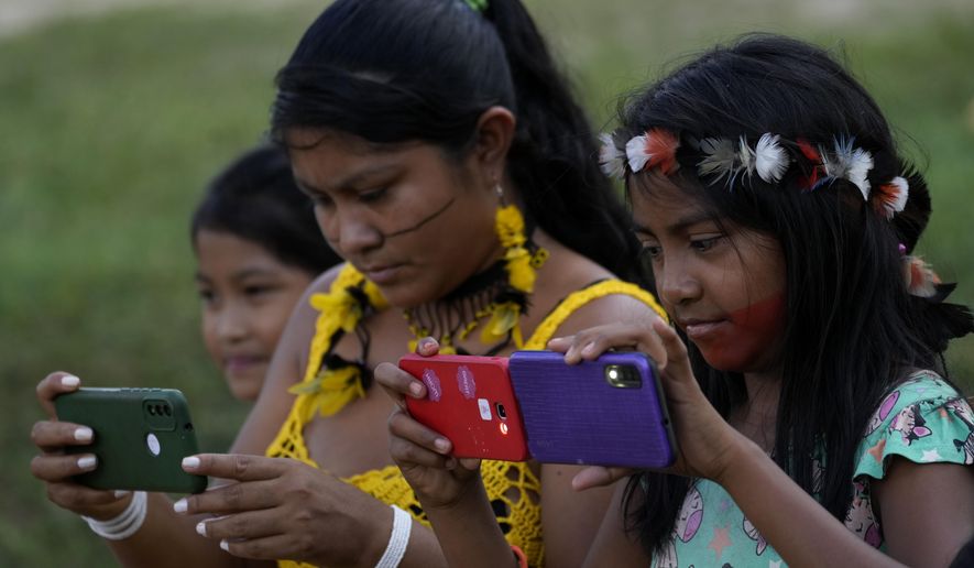 FILE - An Indigenous Tembe mother and daughters take photos on their smartphones outside a school in the Tenetehar Wa Tembe village, located in the Alto Rio Guama Indigenous territory of the Paragominas municipality in the Para state of Brazil, May 30, 2023. (AP Photo/Eraldo Peres, File)