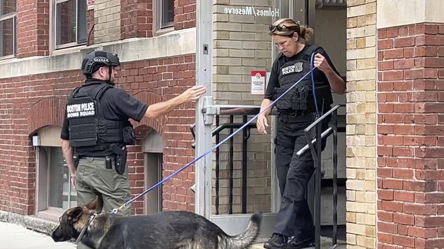 FILE - In a screen grab taken from video, a Boston Police bomb squad officer, left, and a K-9 unit officer, right, depart a building on the campus of Northeastern University, Sept. 14, 2022, in Boston. (AP Photo/Rodrique Ngowi, File)