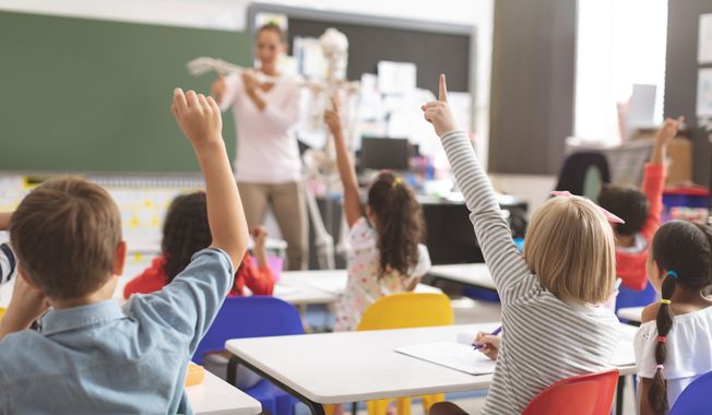 Rear view of kids raising hands while teacher explaining the functioning of human skeleton in classroom at school. File photo credit: wavebreakmedia via Shutterstock.