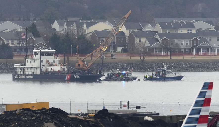 An American Airlines plane passes in the foreground as a member of a dive team and a Coast Guard vessel with a crane work near the wreckage of a Black Hawk helicopter in the Potomac River from Ronald Reagan Washington National Airport, Friday, Jan. 31, 2025, in Arlington, Va. (AP Photo/Alex Brandon)