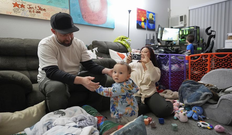 Steve Petersen, left, and his wife Jennifer watch as their daughter Carolynn tries to stand inside their apartment in Campbell, Calif., Wednesday, Jan. 15, 2025. (AP Photo/Godofredo A. Vásquez)