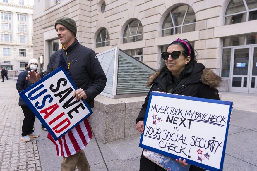 United States Agency for International Development, or USAID contract worker Priya Kathpal, right, and Taylor Williamson, left, who works for a company doing contract work for USAID, carry signs outside the USAID headquarters in Washington, Monday, Feb. 10, 2025. (AP Photo/Manuel Balce Ceneta)