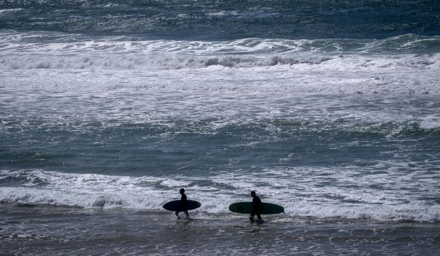 Two surfers walk with their boards on the beach of the Atlantic Ocean in Sines, Portugal, April 1, 2024. (AP Photo/Michael Probst, File)