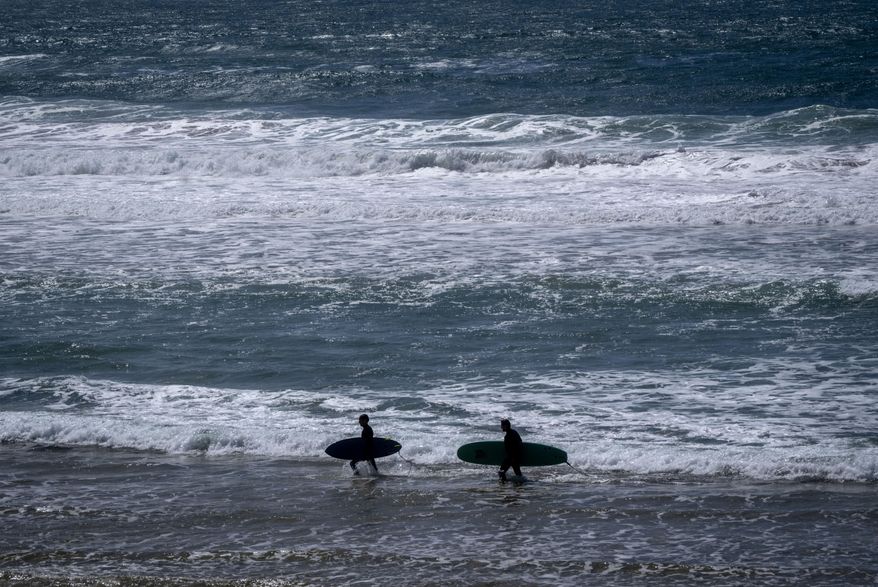 Two surfers walk with their boards on the beach of the Atlantic Ocean in Sines, Portugal, April 1, 2024. (AP Photo/Michael Probst, File)