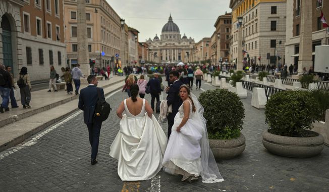 Locals and tourists walk along a main street near St. Peter's Basilica, background, in Rome, Saturday, March 8, 2025. (AP Photo/Francisco Seco)
