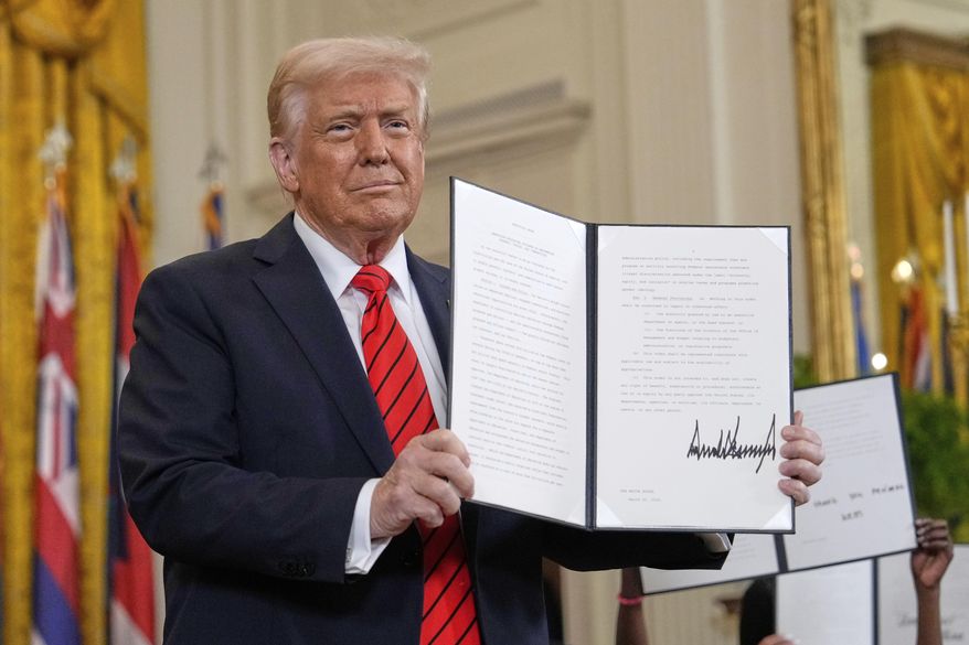 President Donald Trump holds up a signed executive order at an education event in the East Room of the White House in Washington, Thursday, March 20, 2025. (AP Photo/Ben Curtis)