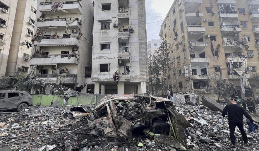 A man walks next to a destroyed car and damaged buildings at the site that was hit by an Israeli airstrike in Dahiyeh, in the southern suburb of Beirut, Lebanon, Friday March 28, 2025.(AP Photo/Hussein Malla)