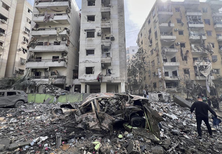 A man walks next to a destroyed car and damaged buildings at the site that was hit by an Israeli airstrike in Dahiyeh, in the southern suburb of Beirut, Lebanon, Friday March 28, 2025.(AP Photo/Hussein Malla)