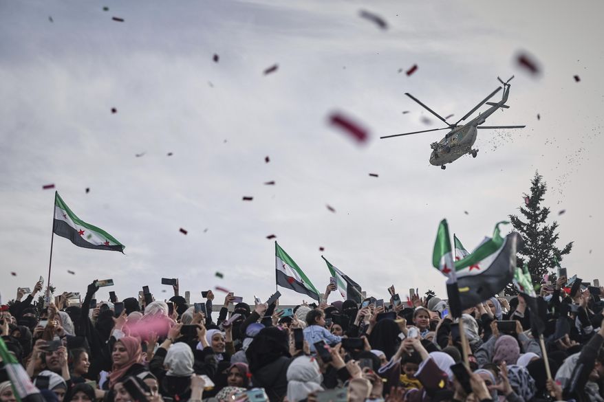 Confetti and flowers are dropped from a military helicopter onto a crowd during a celebration marking the 10th anniversary of the victory of rebel forces over Bashar al-Assad's army in Idlib, Syria, Friday, March 28, 2025. (AP Photo/Ghaith Alsayed)