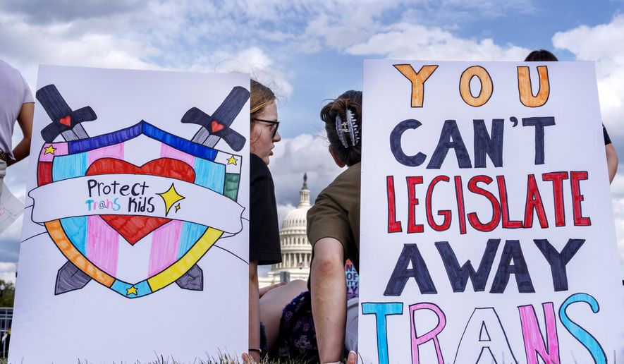 With the U.S Capitol seen between them, people sit by signs saying "protect trans kids," and "you can't legislate away trans" as they attend a rally for the Trans Day of Visibility, on the National Mall, Monday, March 31, 2025, in Washington. (AP Photo/Jacquelyn Martin)