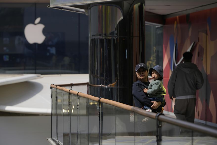 A woman carrying a child stands near Apple and Nike stores in Beijing, China, Friday, April 4, 2025. (AP Photo/Ng Han Guan)