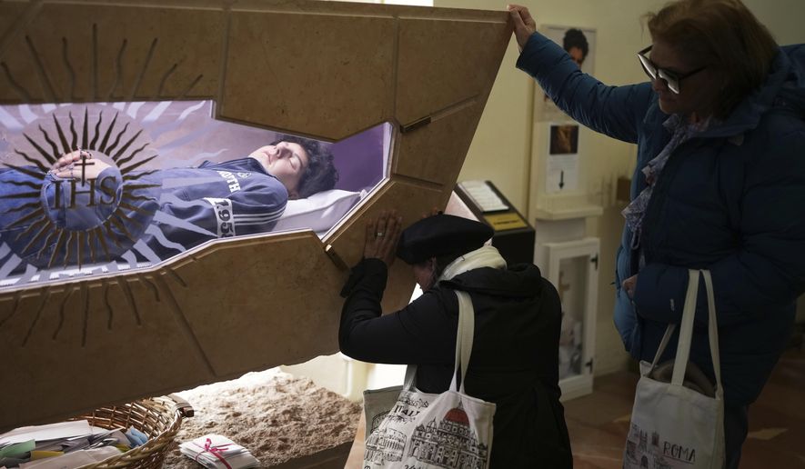 People pray in front of the body of Carlo Acutis, a 15-year-old Italian boy who died in 2006 of leukemia and beatified in 2020, in the Santa Maria Maggiore church in Assisi, Italy, Wednesday, April 2, 2025. (AP Photo/Alessandra Tarantino)