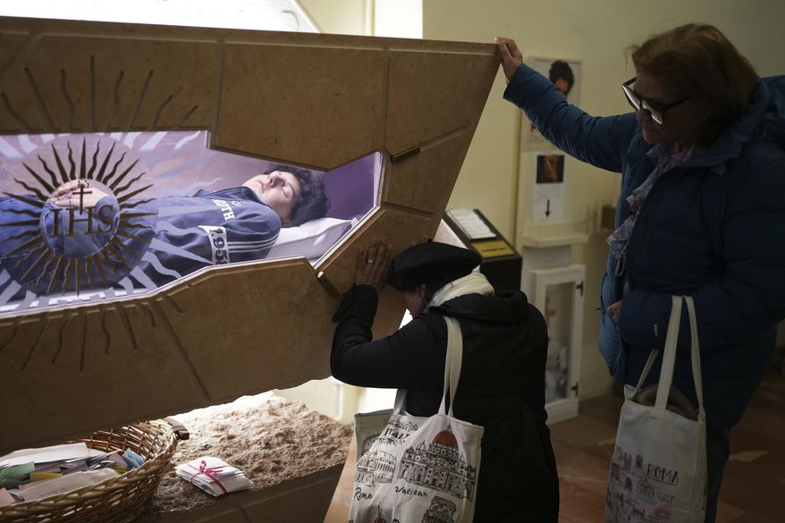 People pray in front of the body of Carlo Acutis, a 15-year-old Italian boy who died in 2006 of leukemia and beatified in 2020, in the Santa Maria Maggiore church in Assisi, Italy, Wednesday, April 2, 2025. (AP Photo/Alessandra Tarantino)