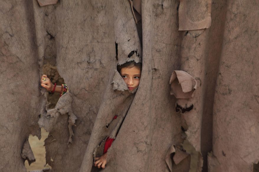 An Afghan refugee girl peers through a torn curtain at the entrance of her home at Kababayan Refugee Camp in Peshawar, Pakistan, Tuesday, April 8, 2025. (AP Photo/Muhammad Sajjad)