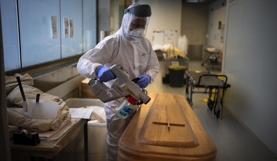 A mortuary worker disinfects a coffin carrying the body of a person who died of COVID-19 ahead of a funeral at Memora mortuary in Girona, Spain, Thursday, Feb. 4, 2021. (AP Photo/Emilio Morenatti, File)