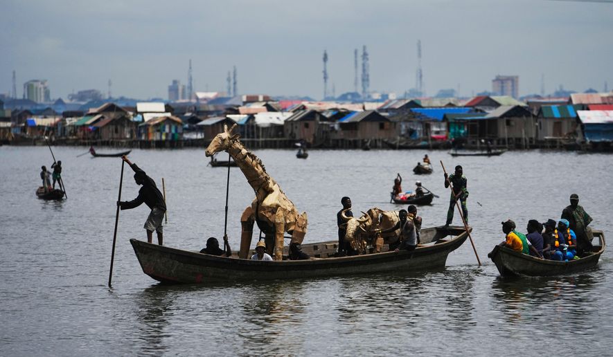 Puppeteers move cardboard animals in canoes at the Makoko Slum in Lagos Nigeria, Saturday, April 19, 2025, as part of "The Herds," a moving theatre performance that started its journey from the Democratic Republic of the Congo to the Arctic Circle in a bid to bring attention to the climate crisis. (AP Photo/Sunday Alamba)