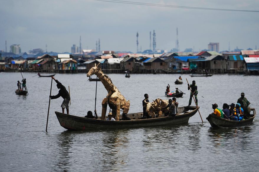 Puppeteers move cardboard animals in canoes at the Makoko Slum in Lagos Nigeria, Saturday, April 19, 2025, as part of "The Herds," a moving theatre performance that started its journey from the Democratic Republic of the Congo to the Arctic Circle in a bid to bring attention to the climate crisis. (AP Photo/Sunday Alamba)
