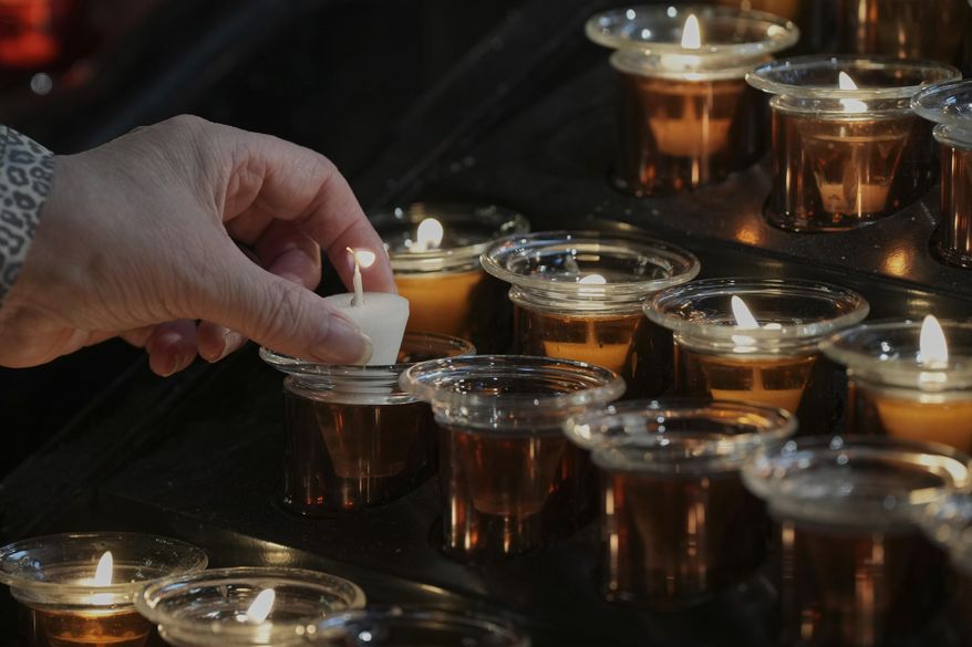 A mourner lights a candle in front of a portrait of Pope Francis inside Westminster Cathedral, in London, Monday, April 21, 2025, following the announcement by the Vatican of the death of Pope Francis. (AP Photo/Alastair Grant)