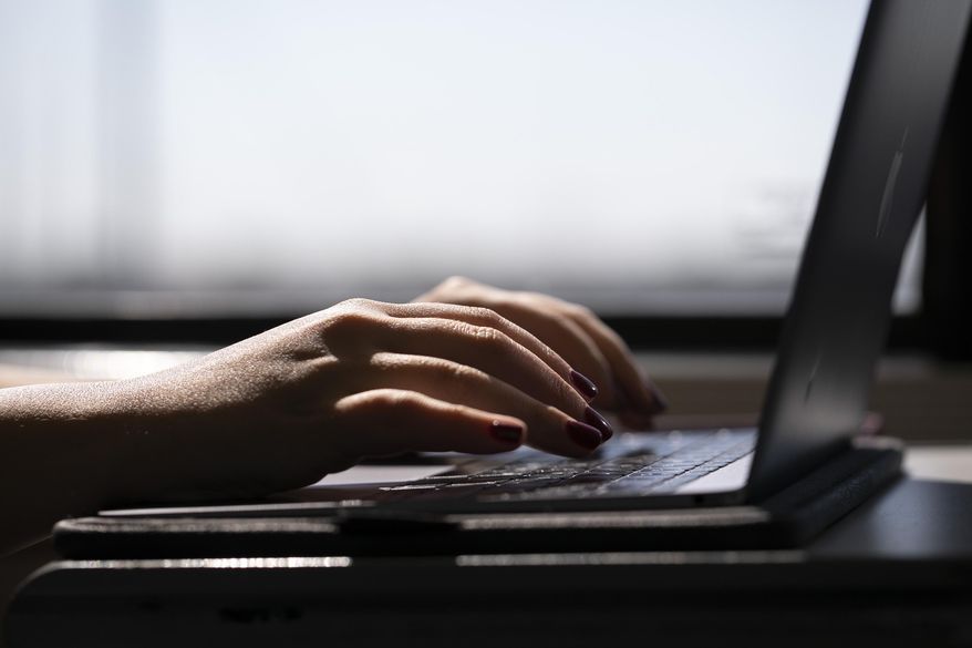 This May 18, 2021, photo shows a woman typing on a laptop on a train in New Jersey. Record numbers of people are starting new businesses, and more and more of them are women and minorities, according to a new study. (AP Photo/Jenny Kane, File)