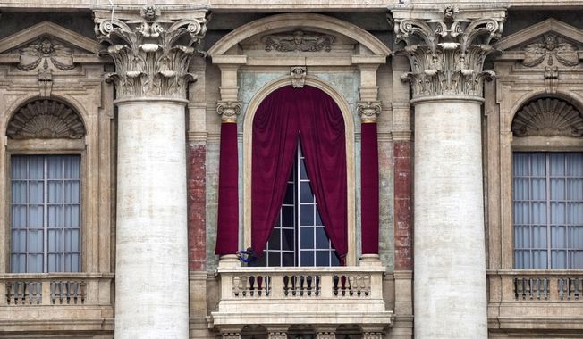 A man gives the last touch to a red drape wrapped around a column of the central lodge of St. Peter's Basilica in Vatican City, Monday, May 5, 2025, before the conclave starting on May 7, where they will elect the 267th pontiff of the Catholic Church. (AP Photo/Gregorio Borgia)