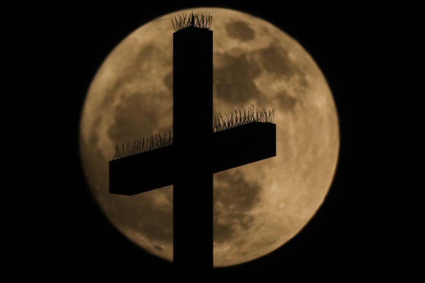 A cross atop the Cathedral of the Immaculate Conception Catholic Church is silhouetted against the rising full moon Sunday, May 11, 2025, in Kansas City, Mo. (AP Photo/Charlie Riedel) ** FILE **