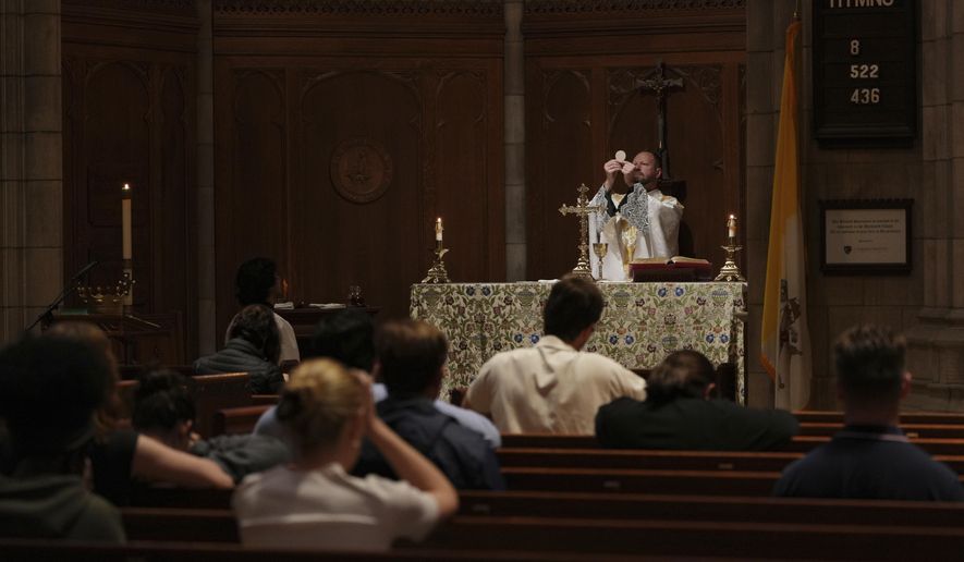 The Rev. Zachary Swantek, Princeton University’s Catholic chaplain and director of the Aquinas Institute - the university’s Catholic campus ministry - raises the host during the Eucharist at a side altar of the school's chapel during a Mass in Princeton, N.J., on Thursday, May 15, 2025. (AP Photo/Luis Andres Henao)