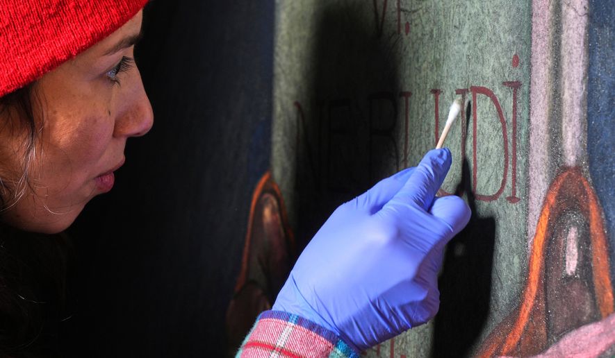 Art conservator Naomi Ruiz uses a cotton swab on a mural by Maxo Vanka that depicts the hand of God handing a tablet to Moses, inside St. Nicholas Croatian Catholic Church in Millvale, Pa., Wednesday, Feb. 19, 2025. (AP Photo/Gene J. Puskar)