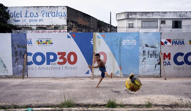 FILE - A boy kicks a soccer ball near signage for the COP30 U.N. Climate Conference in Belem, Brazil, March 23, 2025. (AP Photo/Jorge Saenz, File)
