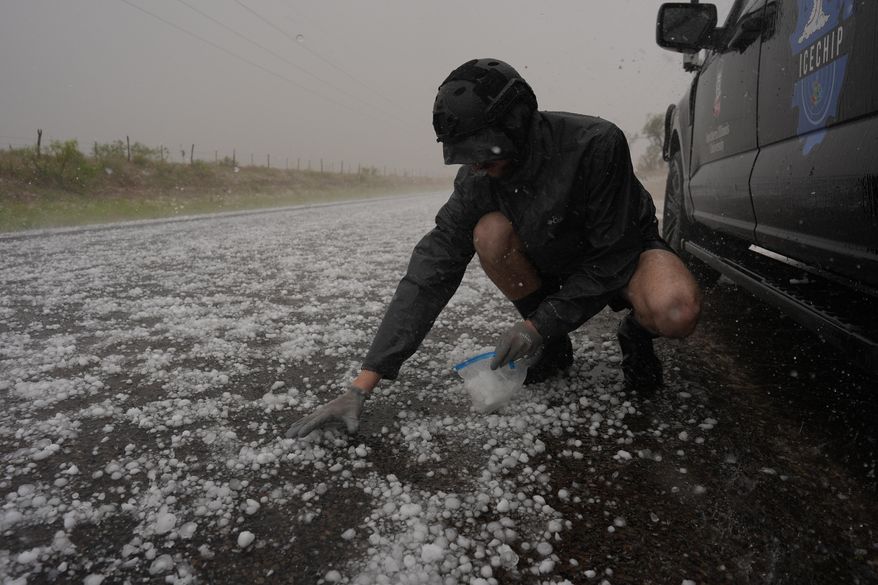 Tony Illenden crouches in a helmet and gloves outside Northern Illinois University's Husky Hail Hunter vehicle to scoop hail into a bag during a storm while on a Project ICECHIP operation Friday, June 6, 2025, in Levelland, Texas. (AP Photo/Carolyn Kaster)
