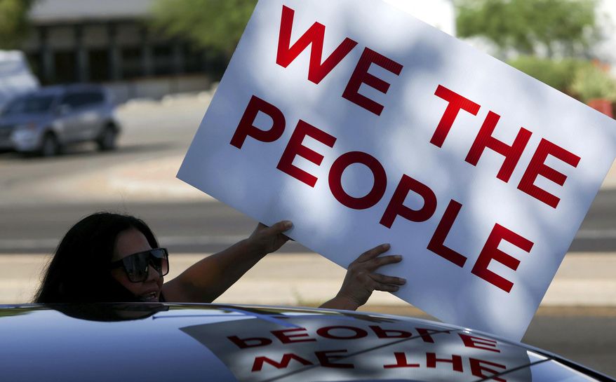 A woman holds a sign that reads "We the people" during a "No Kings" motor march in Tucson, Ariz., Saturday, June 14, 2025. (Grace Trejo/Arizona Daily Star via AP)