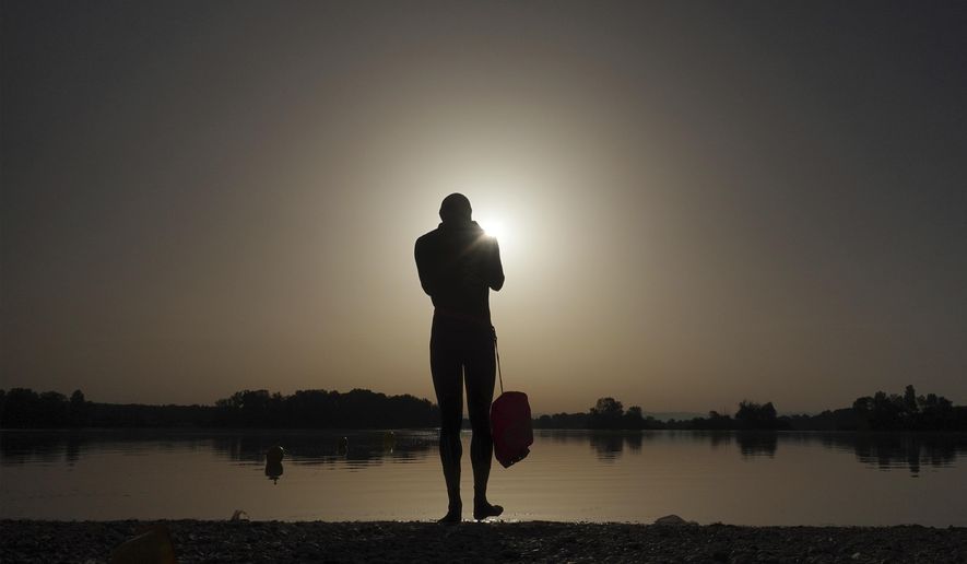 A man prepares to enter the water as the sun rises above the Miribel lake, outside Lyon, France, June 18, 2022. (AP Photo/Laurent Cipriani, File)