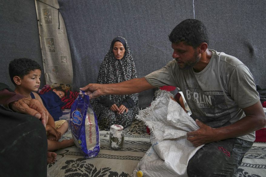 Omar al-Hobi, 43, from Rafah, unpacks a bag of food he collected at a distribution center run by private contractor the Gaza Humanitarian Foundation in the southern Gaza Strip, as he arrives at his family's tent in Khan Younis, Tuesday, June 10, 2025. At left are his children and his wife, Anwaar Saleh.(AP Photo/Abdel Kareem Hana)