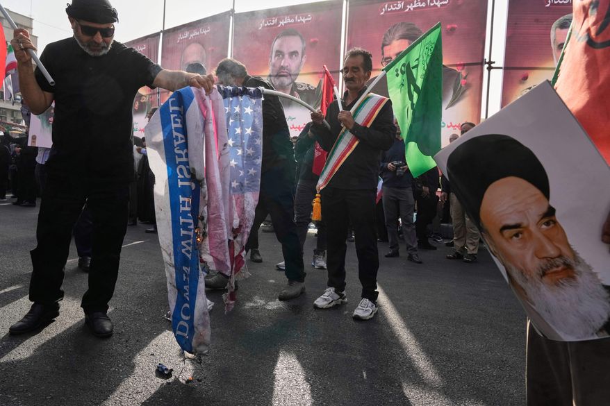 People burn the representations of the U.S. and Israeli flags as a poster of the late Iranian revolutionary founder Ayatollah Khomeini is held at right during the funeral ceremony of Iranian armed forces generals, nuclear scientists and their family members killed in a 12-day war with Israel, in Tehran, Iran, Saturday, June 28, 2025. (AP Photo/Vahid Salemi)