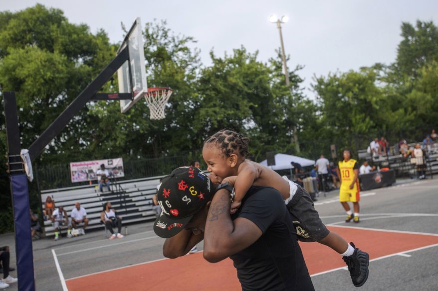 Marco Jackson carries his son Kash Jackson, 1, prior to the Goodman League basketball games Monday, June 30, 2025, in the Barry Farm neighborhood of Washington. (AP Photo/Rod Lamkey, Jr.)