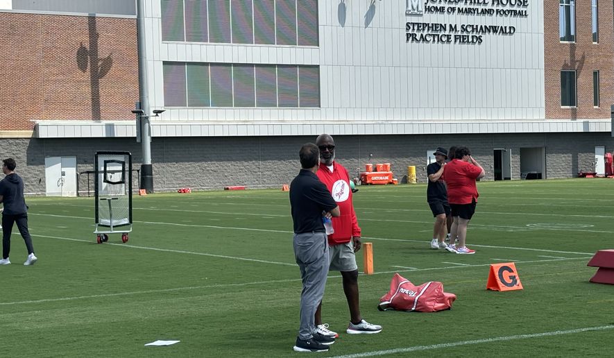 Maryland football coach Mike Locksley (center, in red) speaks with athletic director Jim Smith during the Terrapins' opening practice of training camp, Wednesday, July 30, 2025, in College Park, Md. (George Gerbo/The Washington Times)