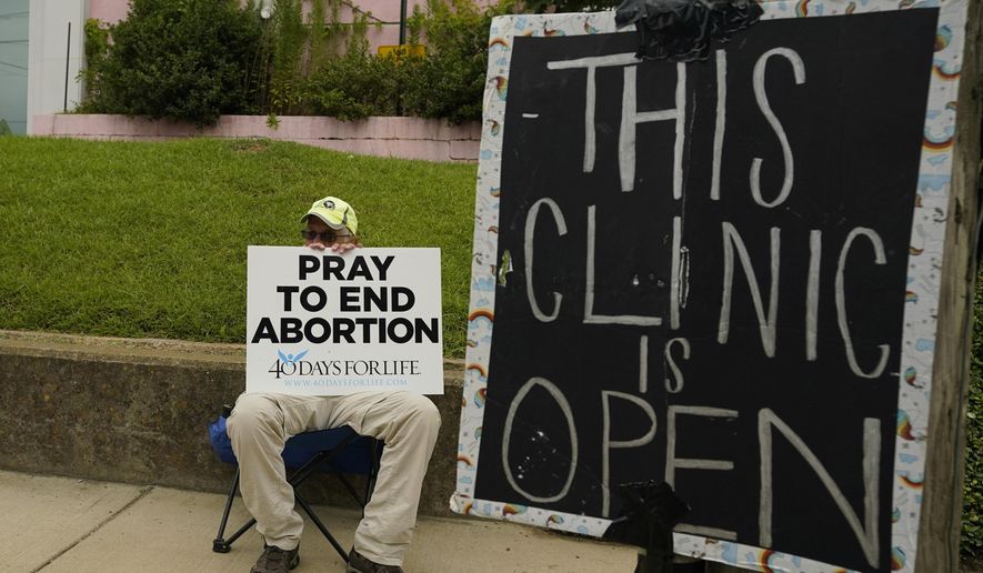 FILE - An anti-abortion supporter sits behind a sign that advises the Jackson Women's Health Organization clinic is still open in Jackson, Miss., July 6, 2022. (AP Photo/Rogelio V. Solis, File)