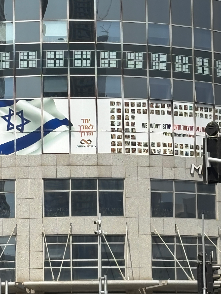 TEL AVIV — Vows to bring home all the hostages abducted by Hamas terrorists on October 7, 2023, are posted everywhere in Tel Aviv. This one is on a building in the area of Menachem Begin Road, where missiles from Iran struck in June of 2025. August 9, 2025. Photo Credit: Cheryl Chumley / The Washington Times