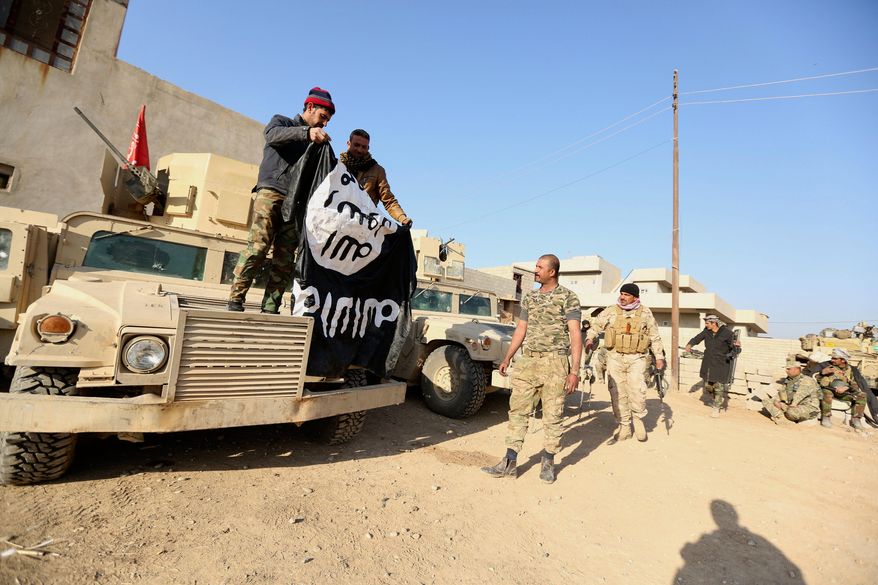 FILE - Iraqi Army soldiers celebrate as they hold a flag of the Islamic State group they captured during a military operation to regain control of a village outside Mosul, Iraq, Tuesday, Nov. 29, 2016. Iraqi officials have begun excavation of what is believed to be a mass grave left behind by the Islamic State extremist group during its rampage across the country a decade ago. (AP Photo/Hadi Mizban, File)