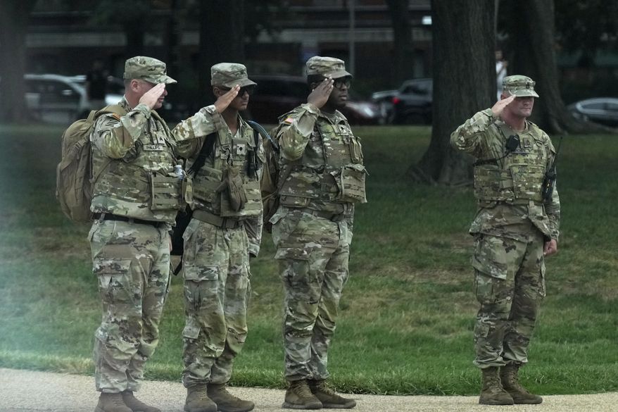 National Guard soldiers salute as the motorcade carrying President Donald Trump, passes by near the White House, Thursday, Aug. 21, 2025, in Washington. (AP Photo/Jacquelyn Martin)